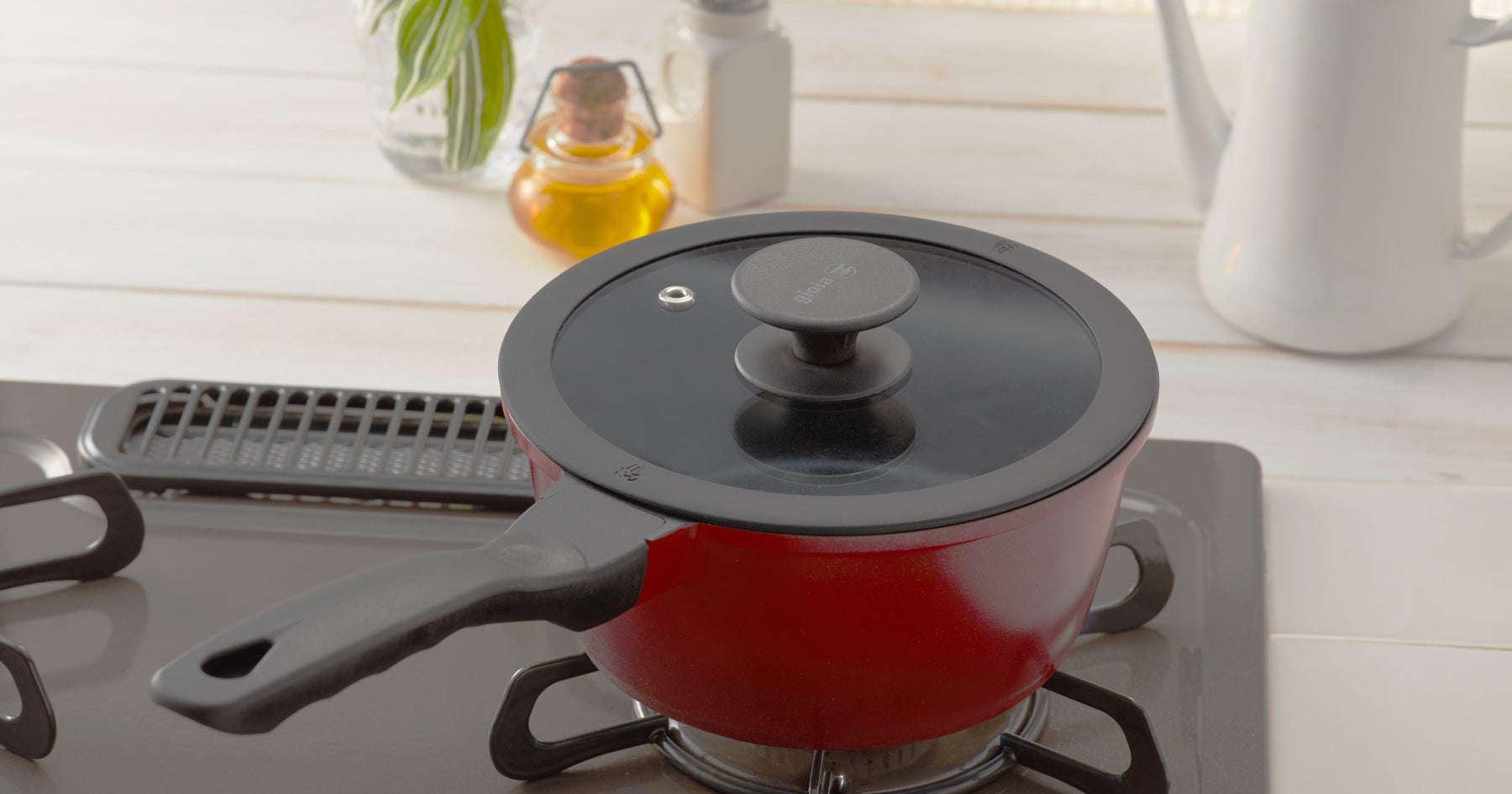 ガスコンロの上に置かれた赤い鍋。透明な蓋が付いており、背景には調味料ボトルや観葉植物が置かれているキッチン。